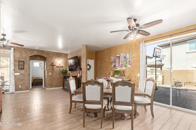 dining room with arched walkways, ceiling fan, wood finish floors, and baseboards