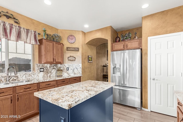 kitchen with tasteful backsplash, stainless steel fridge with ice dispenser, a kitchen island, light stone counters, and a sink