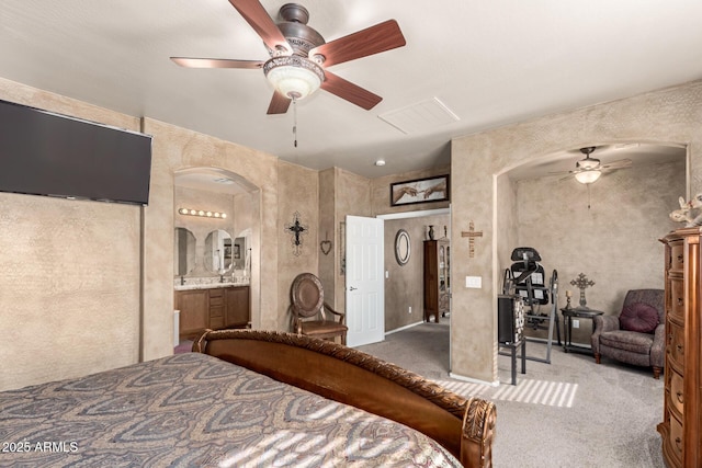 bedroom featuring arched walkways, ceiling fan, ensuite bath, and carpet