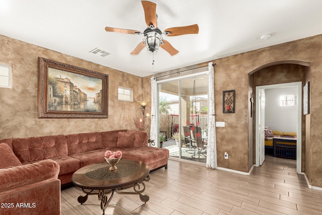 living room featuring light wood finished floors, baseboards, visible vents, and arched walkways