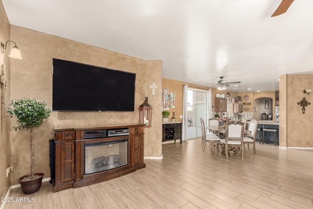 living area featuring ceiling fan, light wood-type flooring, a fireplace, and baseboards