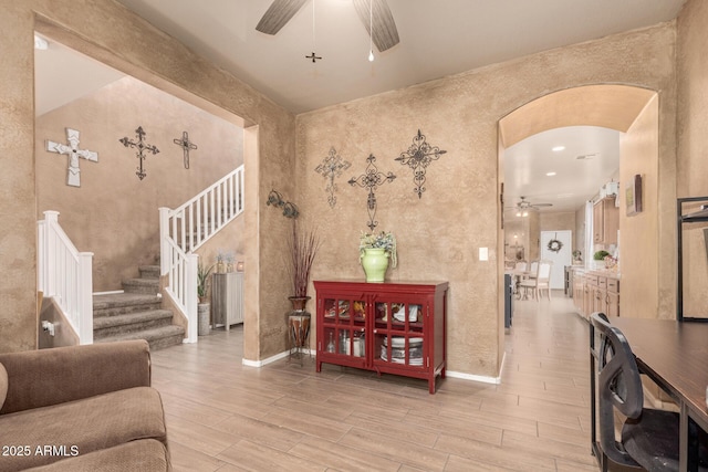 living area with arched walkways, light wood-style flooring, a ceiling fan, baseboards, and stairway