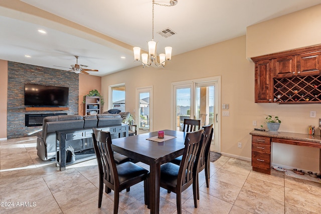 dining area with a stone fireplace and ceiling fan with notable chandelier