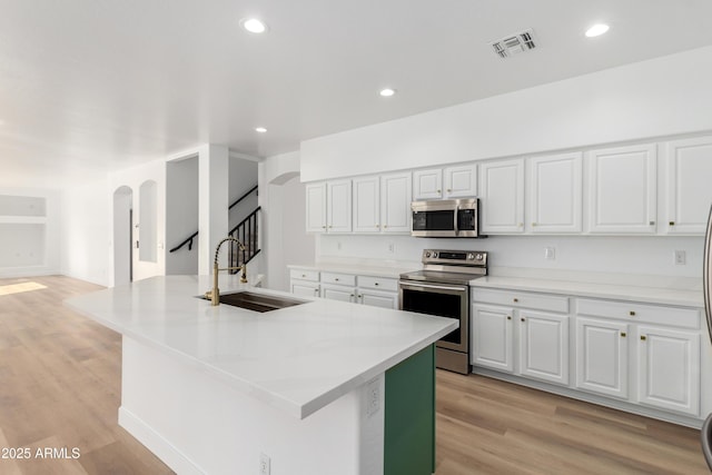 kitchen with white cabinets, stainless steel appliances, a center island with sink, and sink