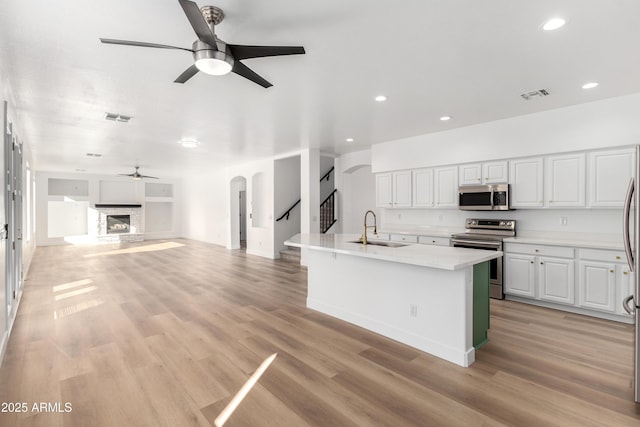 kitchen featuring a kitchen island with sink, white cabinets, a stone fireplace, sink, and appliances with stainless steel finishes