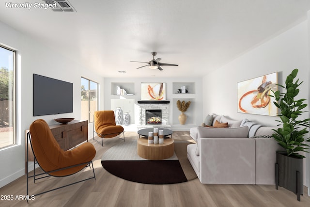 living room featuring a fireplace, light wood-type flooring, built in features, and ceiling fan