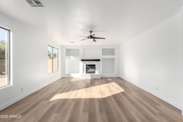 unfurnished living room with built in features, light hardwood / wood-style flooring, a stone fireplace, and ceiling fan