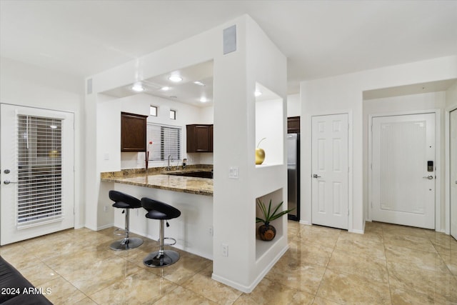 kitchen with stainless steel refrigerator, dark brown cabinetry, light stone counters, kitchen peninsula, and a breakfast bar