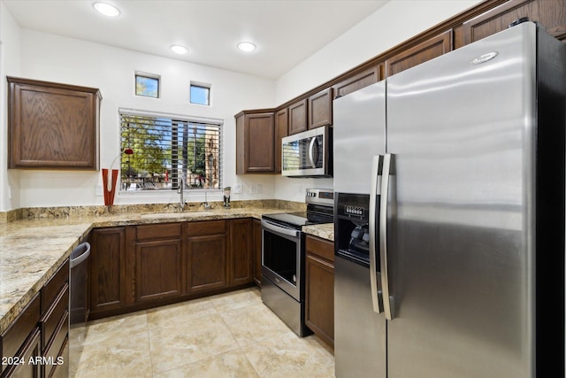 kitchen with dark brown cabinetry, light stone counters, sink, and stainless steel appliances