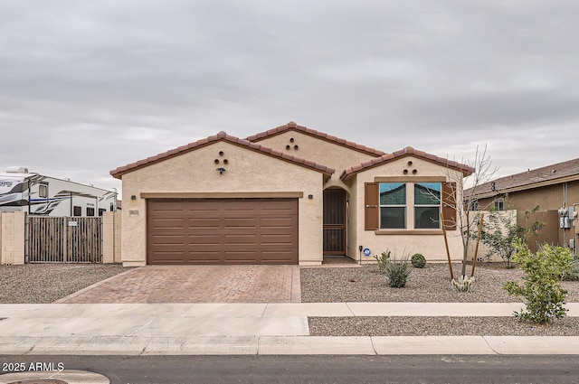 mediterranean / spanish home featuring decorative driveway, stucco siding, an attached garage, fence, and a tiled roof