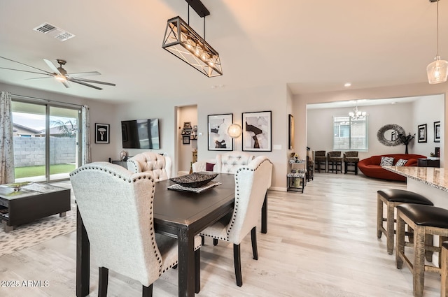 dining space featuring visible vents, light wood-style flooring, and ceiling fan with notable chandelier