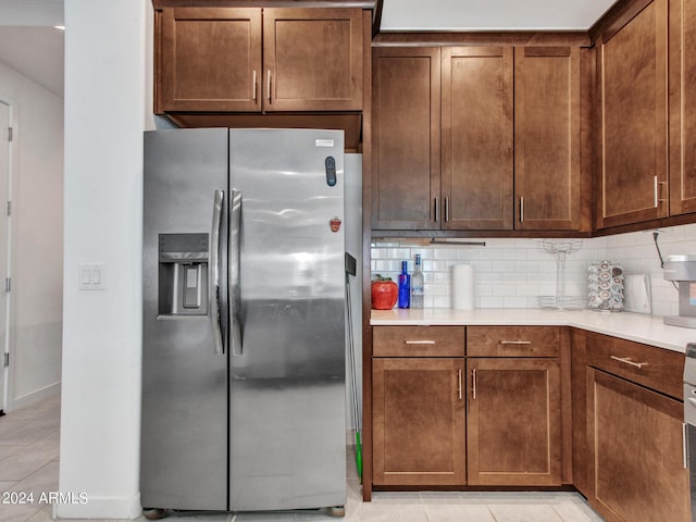 kitchen with light tile patterned floors, light countertops, decorative backsplash, and stainless steel fridge