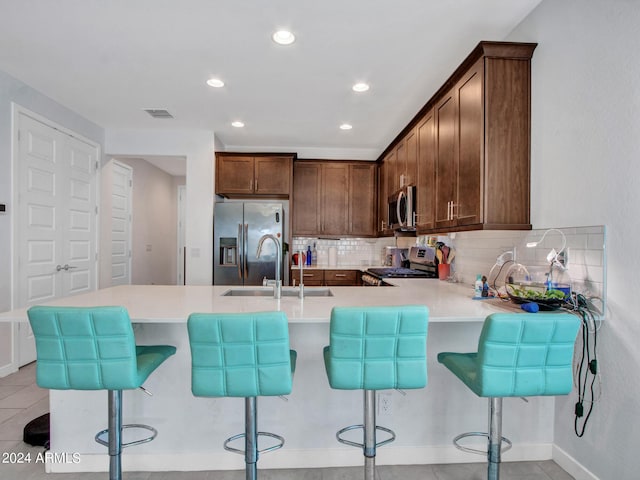 kitchen featuring a peninsula, light countertops, a sink, stainless steel appliances, and decorative backsplash