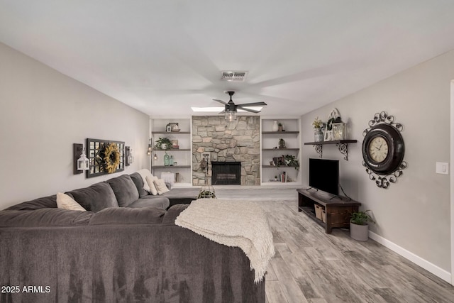 living room with visible vents, baseboards, ceiling fan, light wood-type flooring, and a stone fireplace