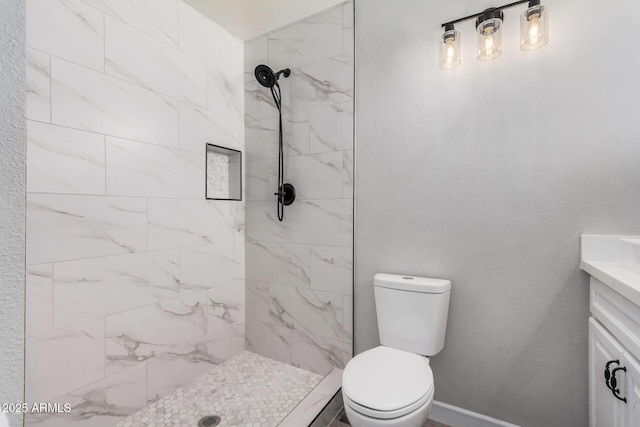 bathroom featuring toilet, tiled shower, vanity, and a textured wall