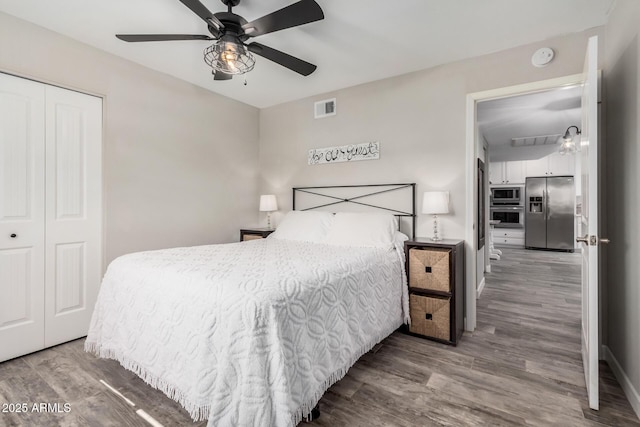 bedroom featuring visible vents, a ceiling fan, wood finished floors, a closet, and stainless steel fridge with ice dispenser