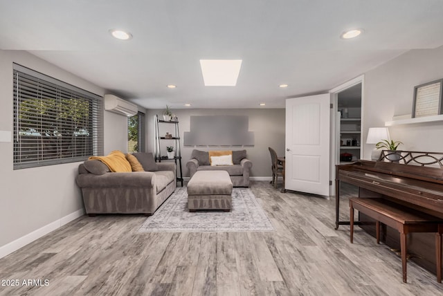 living room featuring wood finished floors, baseboards, an AC wall unit, and a skylight