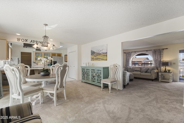 dining area featuring a textured ceiling, light colored carpet, and a notable chandelier