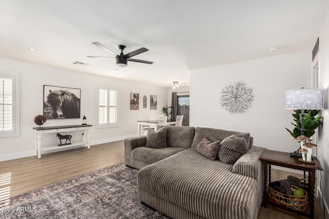 living area with ceiling fan, wood finished floors, visible vents, and baseboards