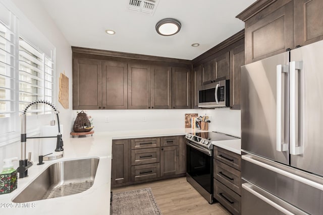 kitchen featuring stainless steel appliances, visible vents, light wood-style flooring, a sink, and dark brown cabinetry