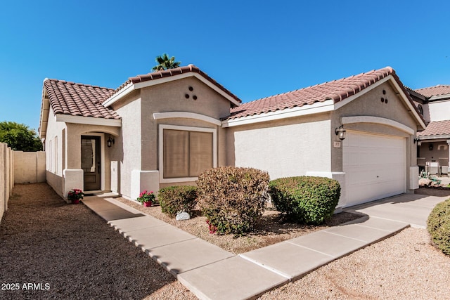 mediterranean / spanish house featuring a tile roof, fence, an attached garage, and stucco siding