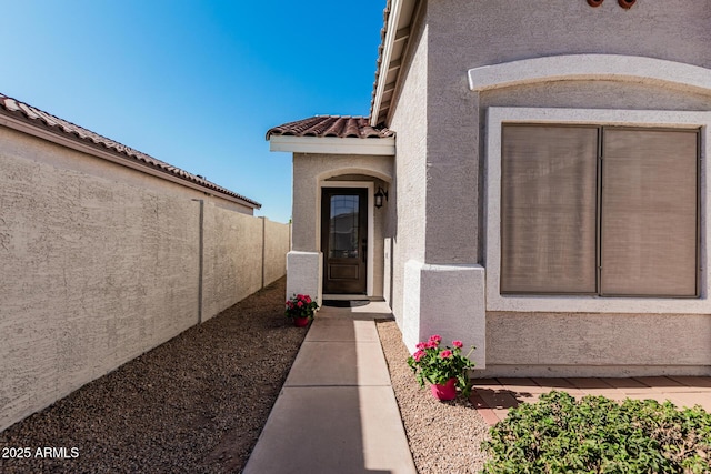 property entrance with a tile roof, fence, and stucco siding