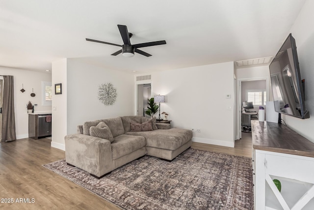 living room with ceiling fan, wood finished floors, visible vents, and baseboards