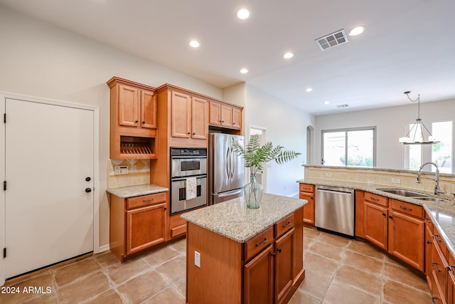 kitchen with appliances with stainless steel finishes, light stone counters, a kitchen island, and sink