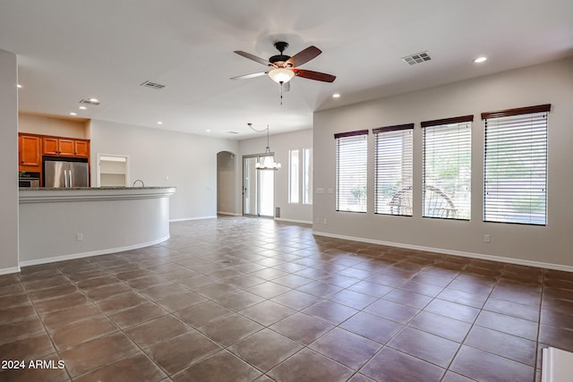 unfurnished living room with dark tile patterned flooring and ceiling fan with notable chandelier