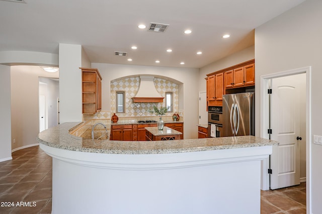 kitchen featuring kitchen peninsula, light stone countertops, backsplash, stainless steel appliances, and sink