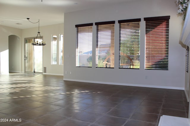 spare room with dark tile patterned floors and a chandelier