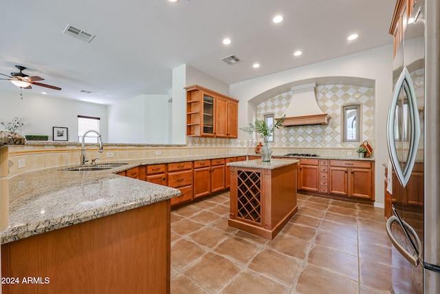 kitchen with stainless steel refrigerator, sink, tasteful backsplash, kitchen peninsula, and custom exhaust hood