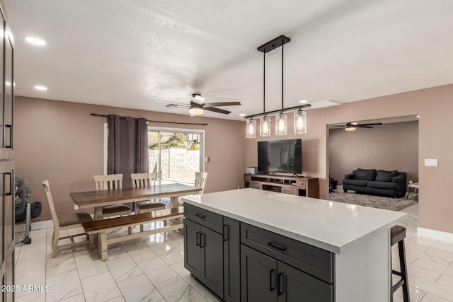 kitchen with ceiling fan, a center island, a textured ceiling, and decorative light fixtures