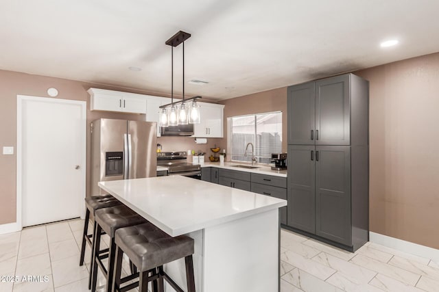 kitchen featuring white cabinetry, sink, a center island, hanging light fixtures, and appliances with stainless steel finishes