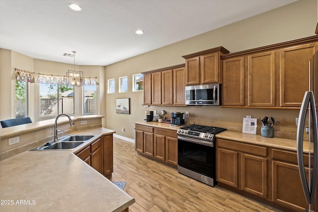 kitchen with an inviting chandelier, sink, appliances with stainless steel finishes, decorative light fixtures, and light hardwood / wood-style floors