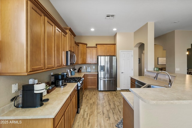 kitchen with sink, an island with sink, stainless steel appliances, and light wood-type flooring