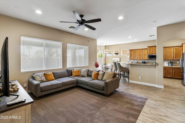 living room featuring ceiling fan with notable chandelier and light hardwood / wood-style flooring