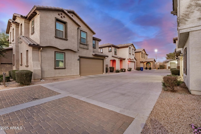 view of front of property featuring decorative driveway, stucco siding, an attached garage, a residential view, and a tiled roof