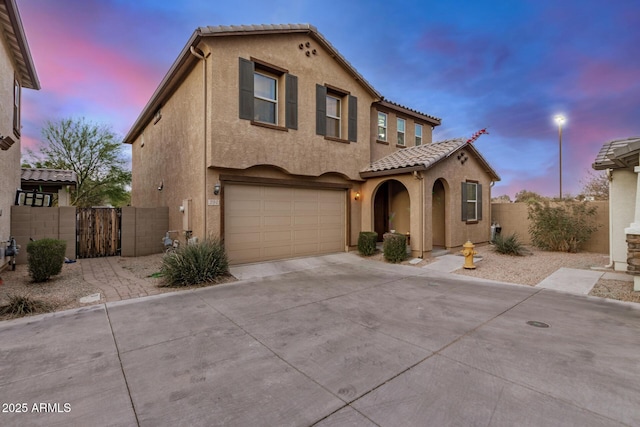 mediterranean / spanish-style house with a garage, a tile roof, fence, and stucco siding