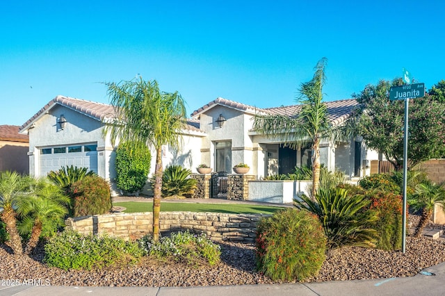 mediterranean / spanish-style house featuring a garage, a fenced front yard, stucco siding, and a tiled roof