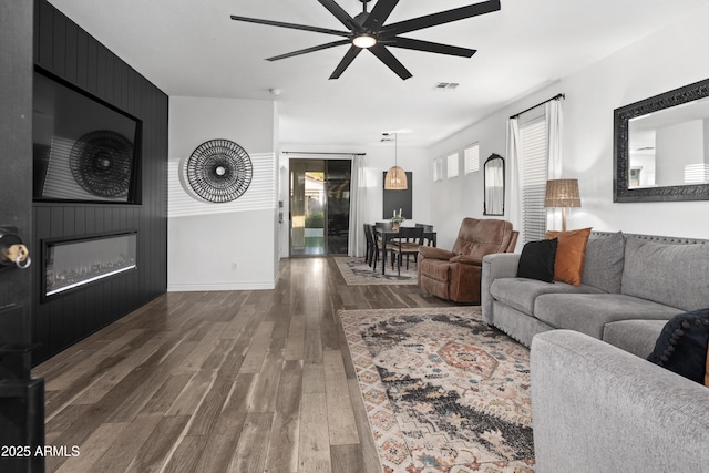 living room with a fireplace, a ceiling fan, baseboards, wood finished floors, and visible vents