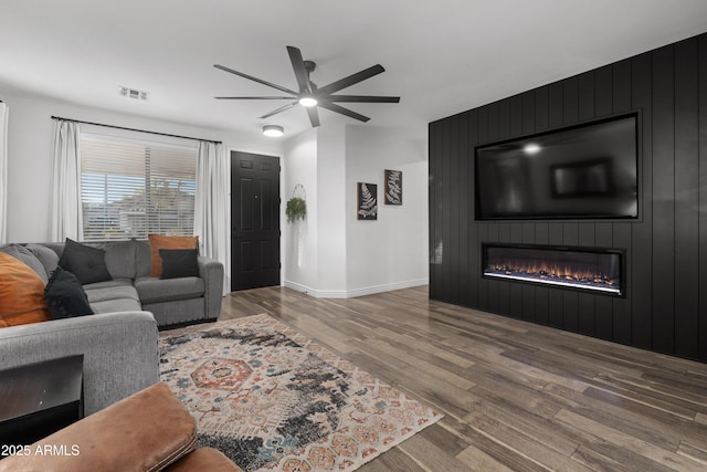living area with ceiling fan, a fireplace, baseboards, wood finished floors, and visible vents