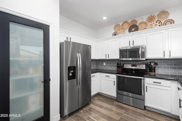 kitchen with decorative backsplash, wood finished floors, white cabinets, dark stone countertops, and stainless steel appliances