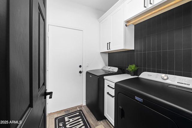 laundry area featuring separate washer and dryer, cabinet space, and wood finished floors