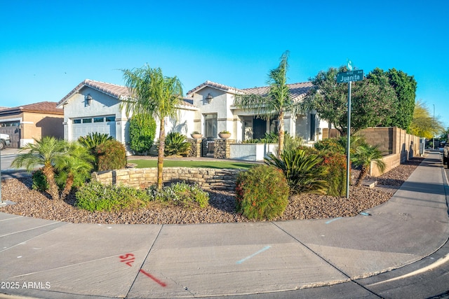 mediterranean / spanish home featuring fence, a tiled roof, an attached garage, and stucco siding