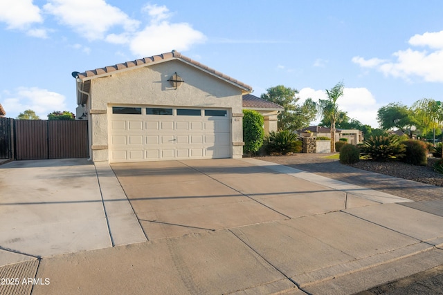 view of front facade featuring fence, a garage, stucco siding, a gate, and driveway