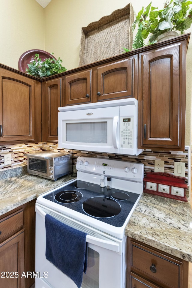 kitchen featuring decorative backsplash, light stone countertops, and white appliances