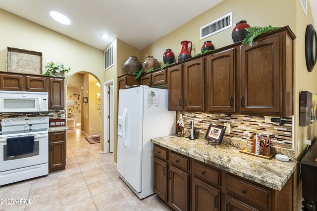 kitchen featuring white appliances, backsplash, light stone countertops, light tile patterned flooring, and dark brown cabinetry