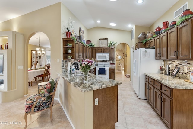 kitchen with lofted ceiling, white appliances, tasteful backsplash, light stone counters, and kitchen peninsula