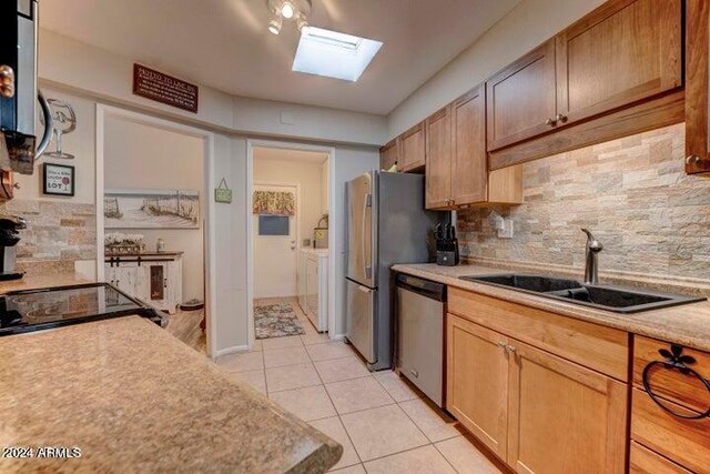 kitchen featuring a skylight, light tile patterned floors, backsplash, appliances with stainless steel finishes, and sink